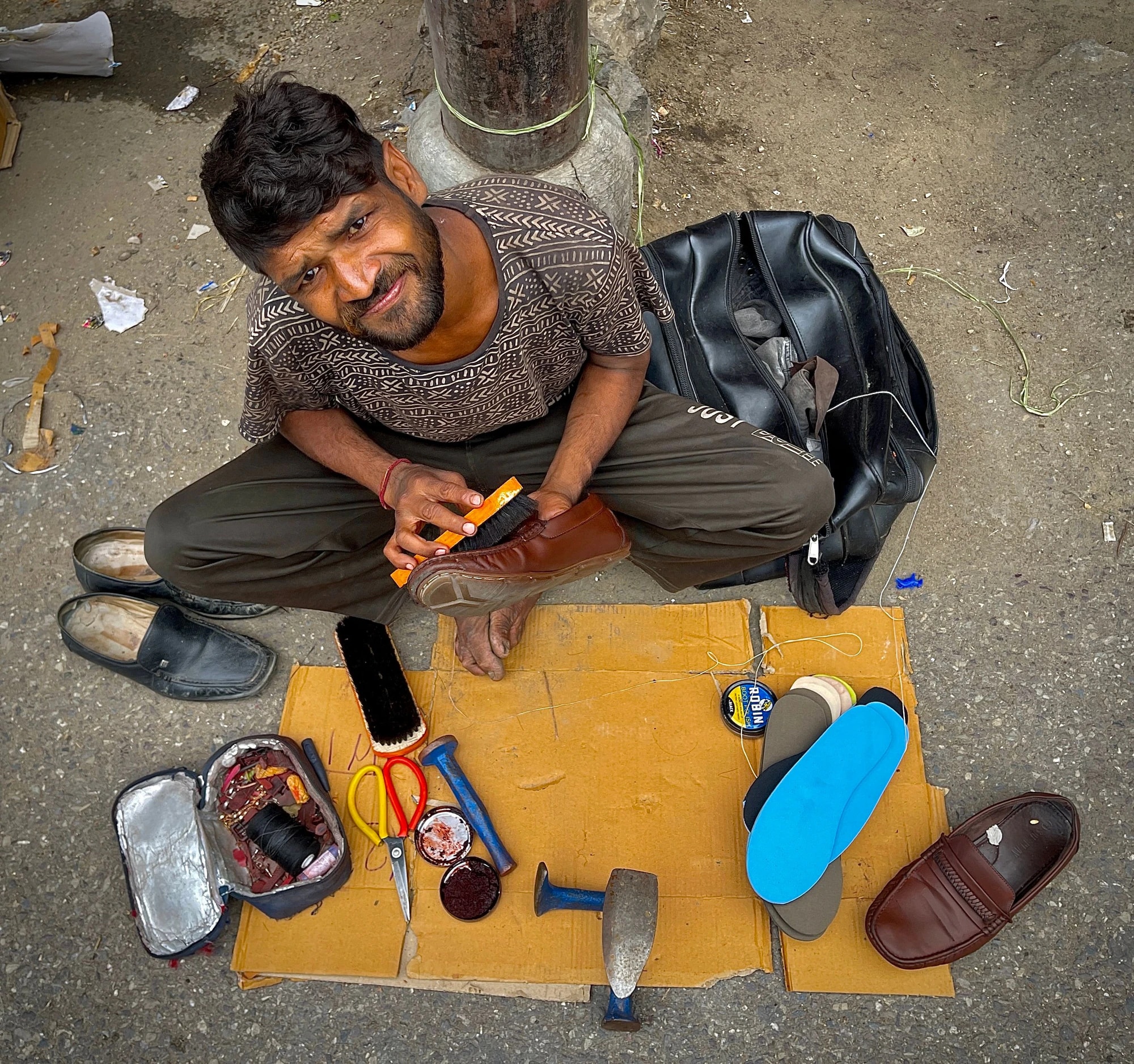 A street cobbler — a mochi — smiling as he repairs footwear