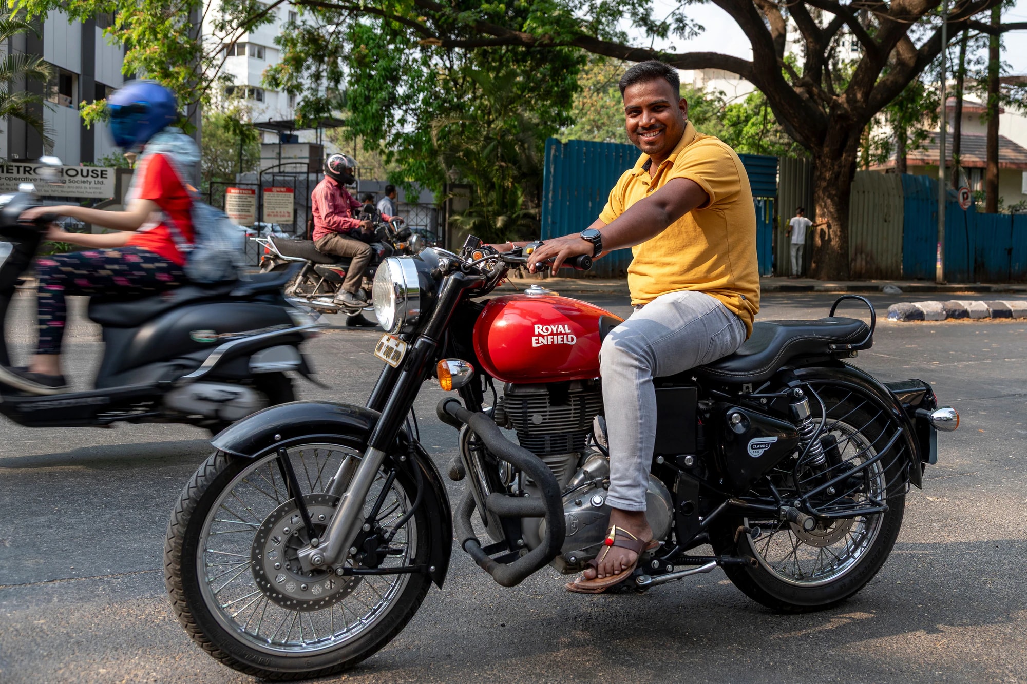 A smiling man sitting on a red motorbike on a city street